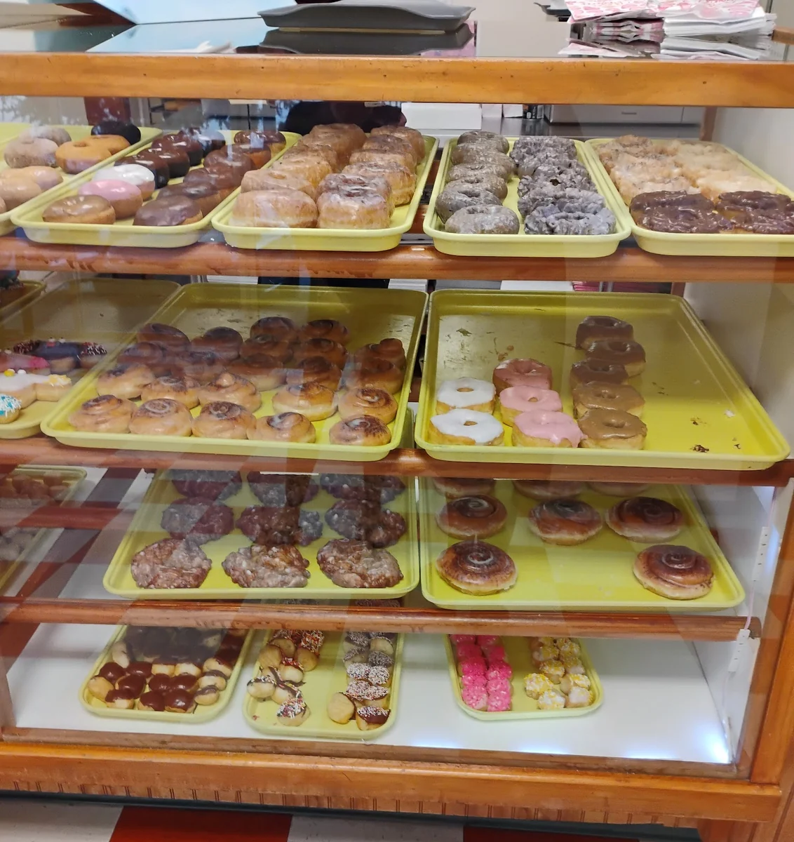Display case full of glazed, chocolate, sprinkle, and cake doughnuts in yellow trays